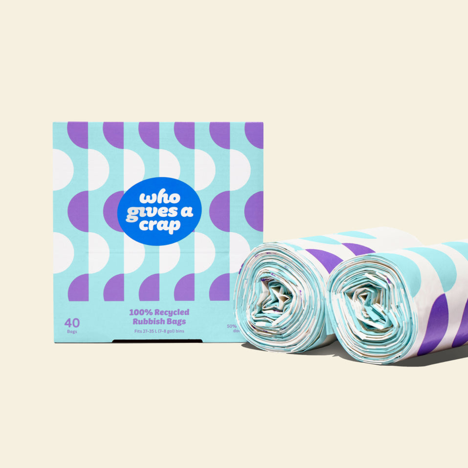 Two rolls and a box of Who Gives a Crap medium recycled garbage bags with purple and blue packaging
