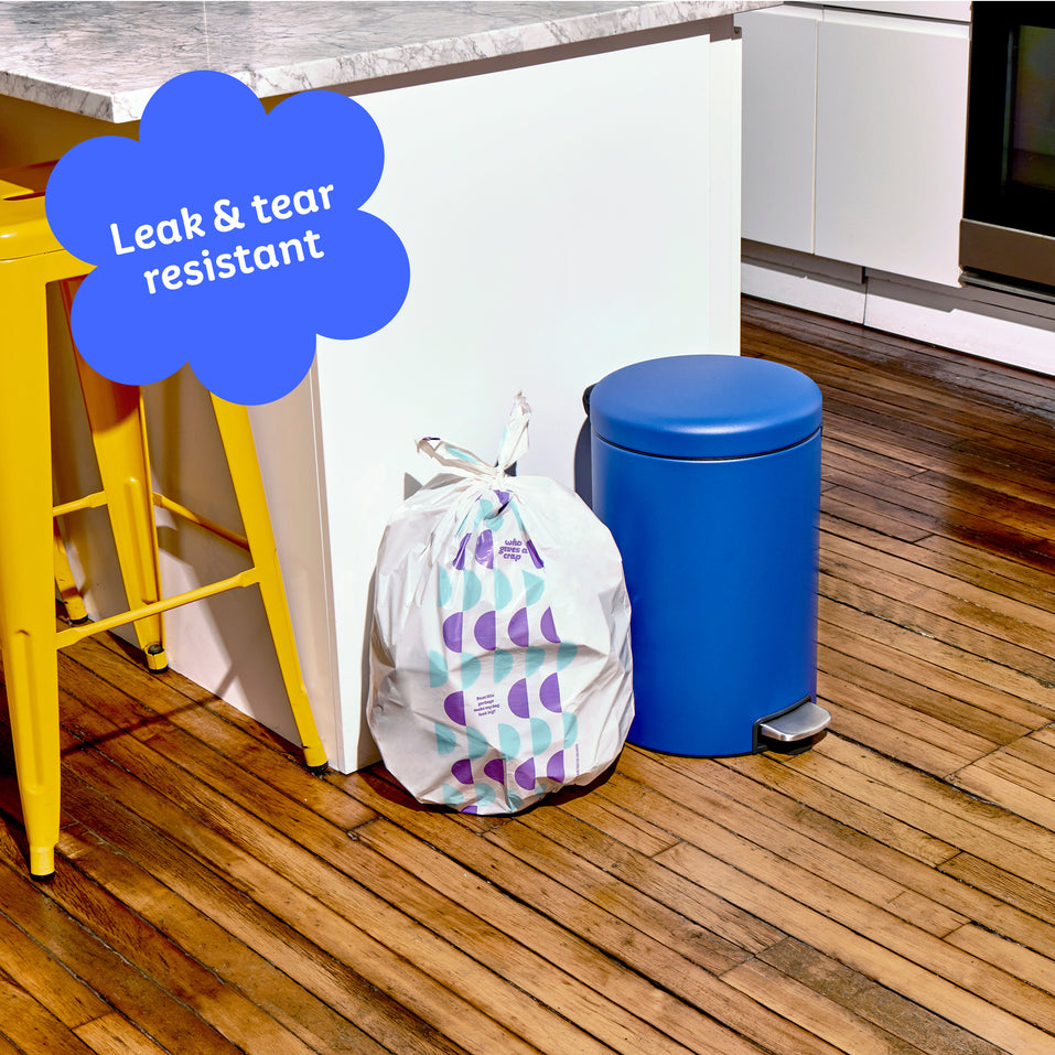Who Gives a Crap medium recycled garbage bag sits full next to kitchen bin. Caption in corner reads ‘Leak & tear resistant’.