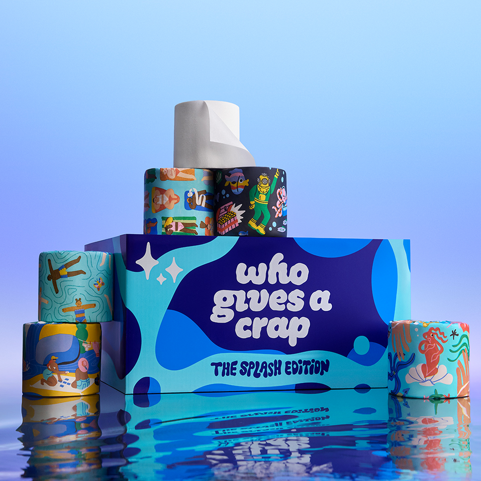 The Who Gives A Crap Splash Edition box and illustrated bamboo toilet rolls reflected in water, with a collection of uniquely designed rolls on display