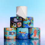 A pyramid stack of Who Gives A Crap Splash Edition bamboo toilet rolls featuring ocean and water-themed illustrations including mermaids, sea creatures and swimmers