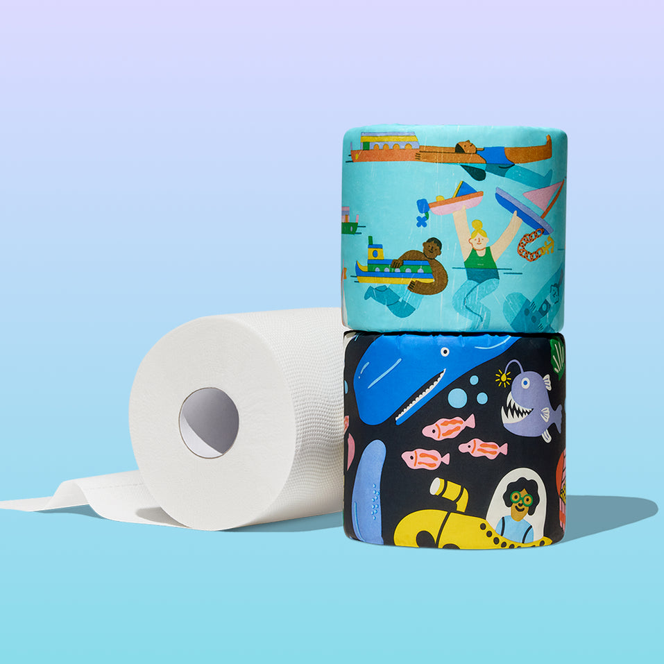 Two stacked Who Gives A Crap Splash Edition illustrated rolls beside an unrolled white bamboo toilet paper roll, showing water activities and deep sea creature designs