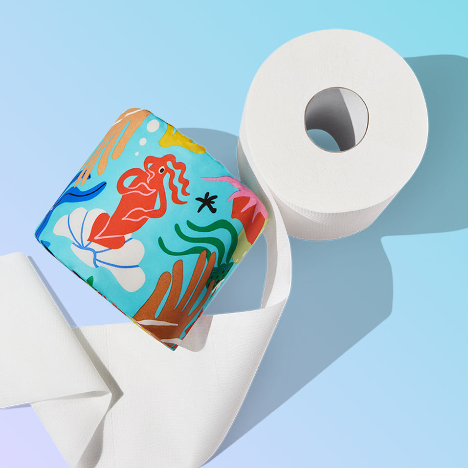 A Who Gives A Crap Splash Edition roll featuring a bold red mermaid illustration resting against an unwrapped white bamboo toilet paper roll