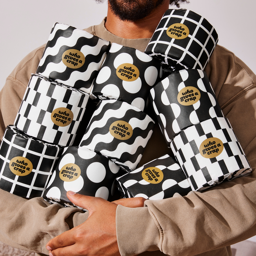 Man holds armful of patterned Who Gives a Crap recycled toilet paper rolls