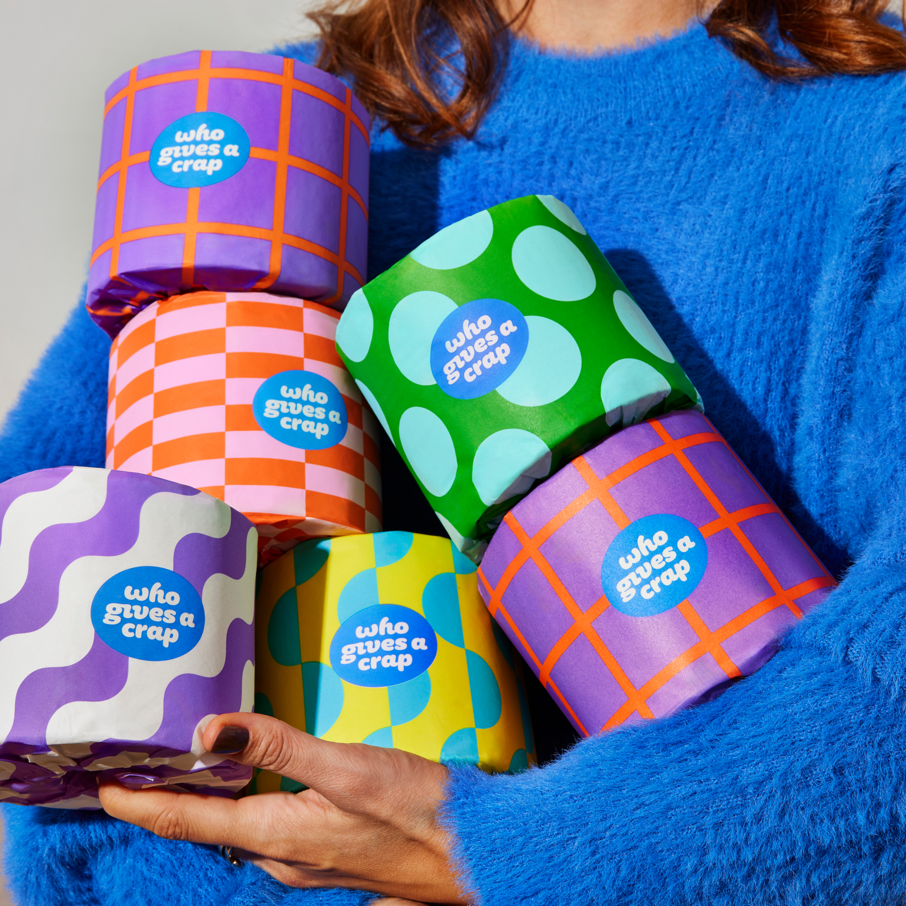 Woman holds handful of colourful Who Gives a Crap recycled toilet paper rolls