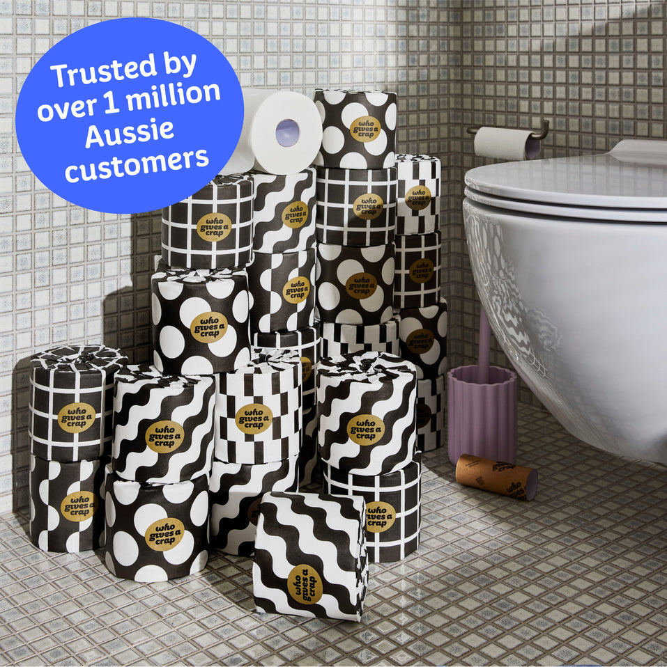 Several rolls of wrapped and unwrapped Premium Toilet Paper sits on the bathroom floor next to a toilet. Copy over the image reads ‘Trusted by over 1 million Aussie customers’.