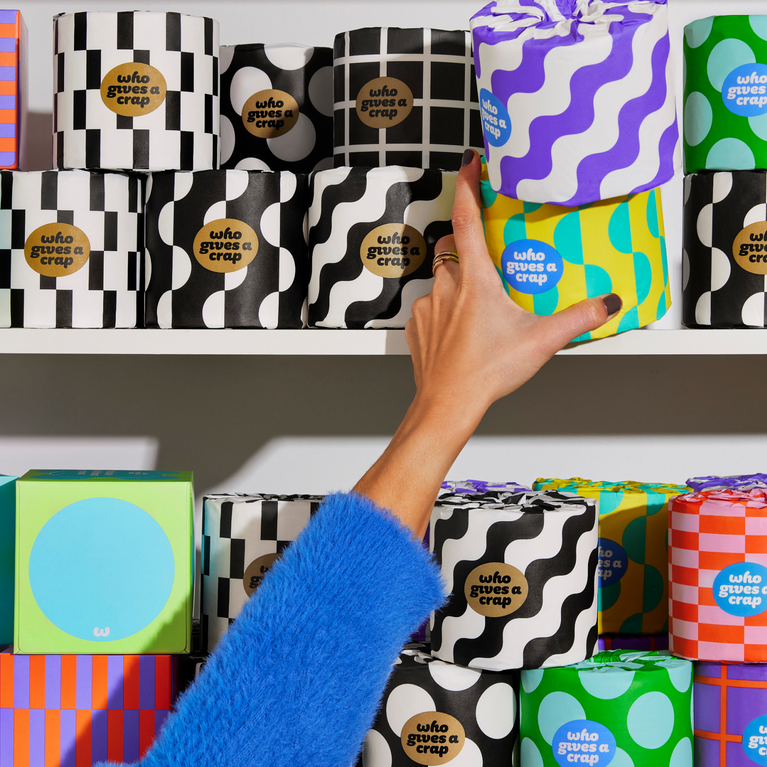 Hand reaching to shelf with colourfully wrapped eco-friendly toilet paper and tissue boxes.