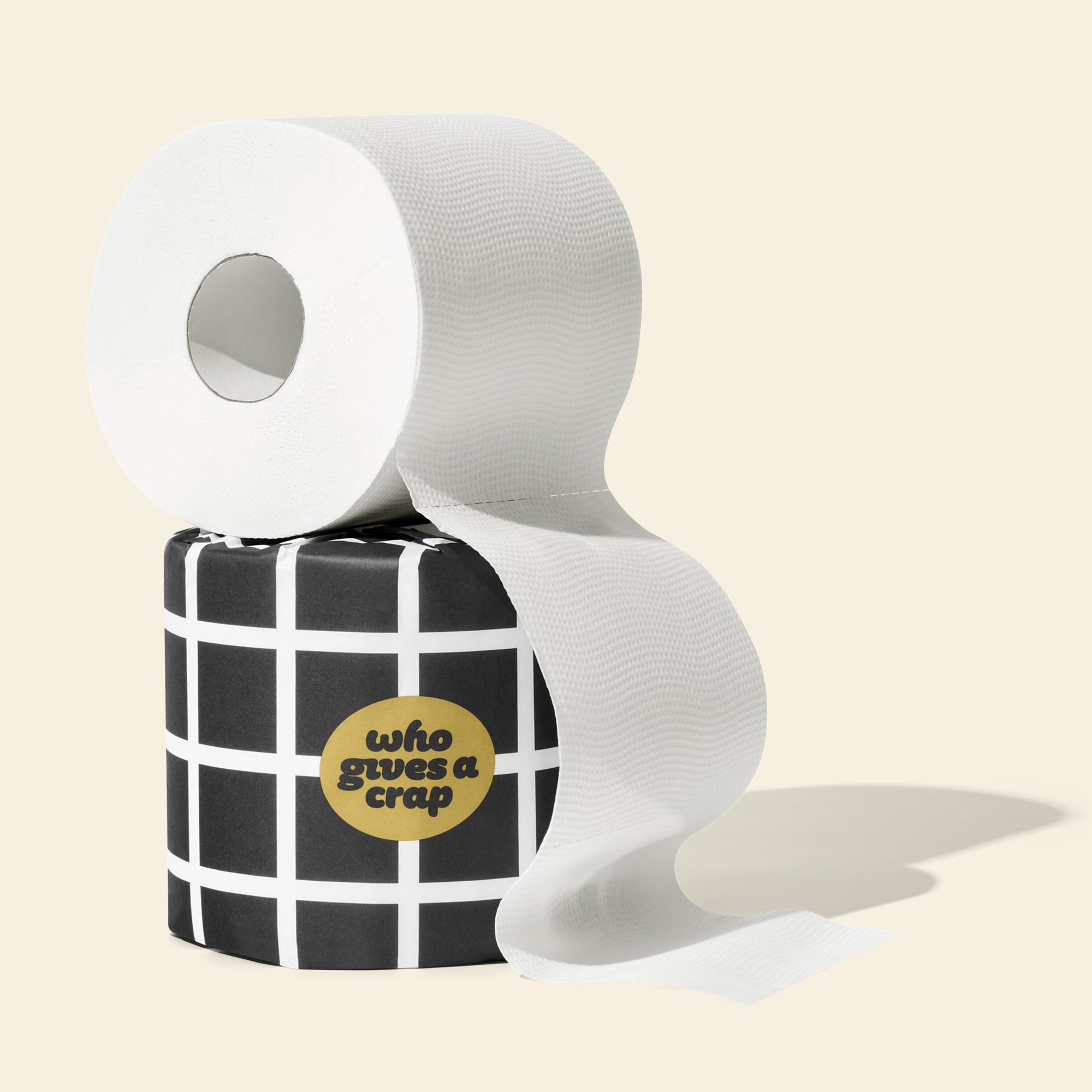 Single roll of open Who Gives a Crap bamboo toilet paper sitting on top of a roll wrapped in black and white packaging