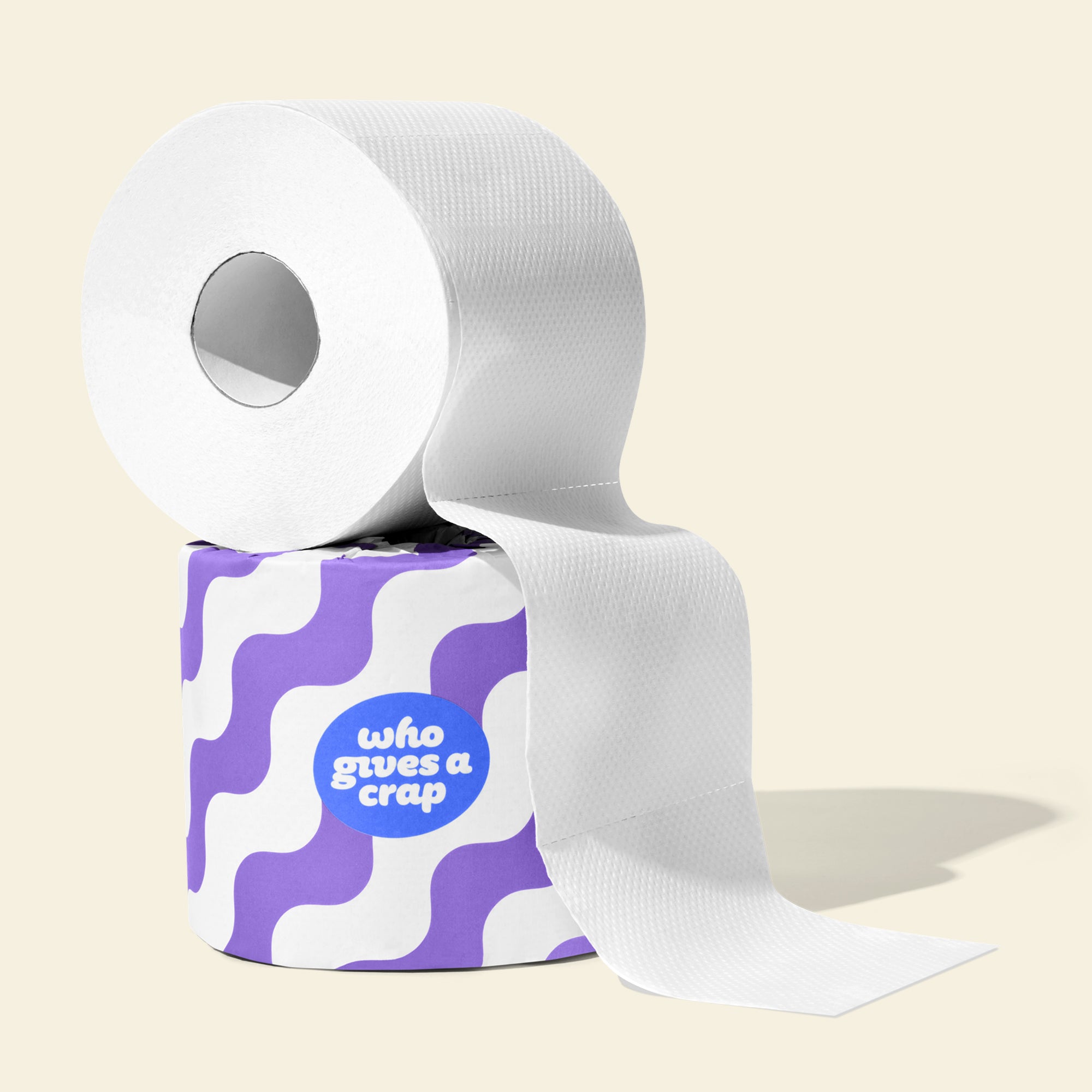 Single roll of open Who Gives a Crap recycled toilet paper sitting on top of a roll wrapped in colourful packaging