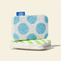 A Who Gives A Crap blue polka dot scrubbing sponge scourer stacked on top of a green striped scourer sponge, showing the soft sponge side and natural loofah scrubbing side