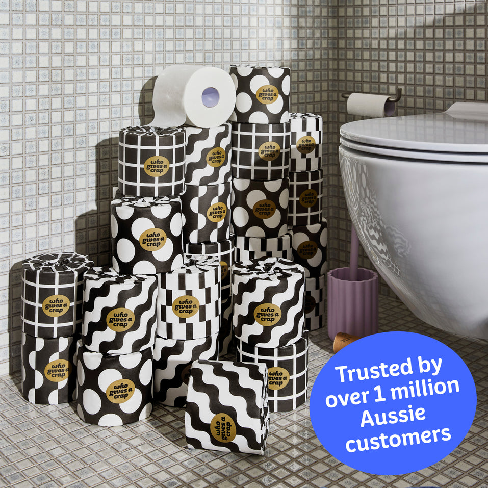 Several rolls of wrapped and unwrapped Premium Toilet Paper sits on the bathroom floor next to a toilet. Copy over the image reads ‘Trusted by over 1 million Aussie customers’.