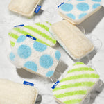 Multiple Who Gives A Crap scourer sponges scattered in soapy water, displaying the blue polka dot, green stripe and natural loofah sides