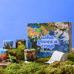 A box with a satellite image of earth, surrounded by stacks of eco-friendly toilet paper rolls wrapped in photography of animals and nature placed ontop of a in a mossy scene