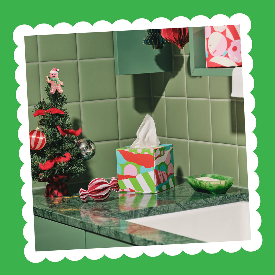 A festive Perfect Pair tissue box on a green marble bench next to a Christmas tree, a candy and a small dish.