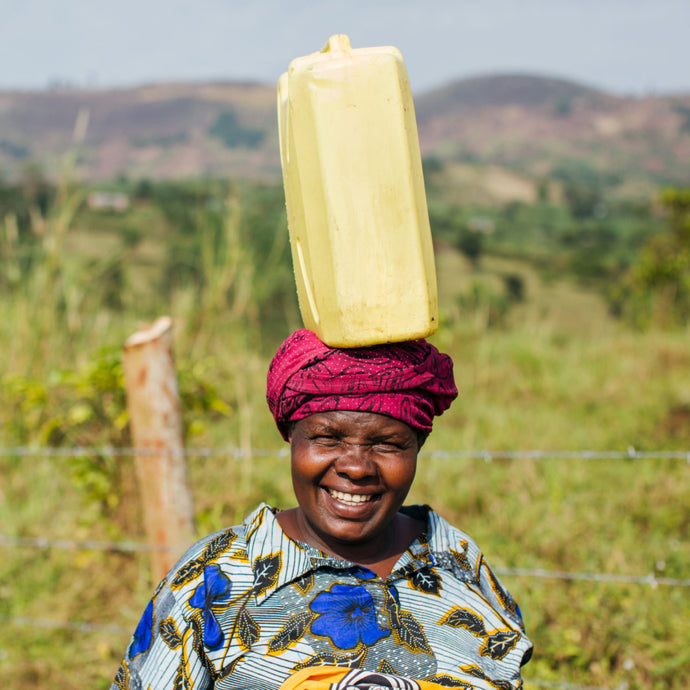 Person balancing a large water gallon on their head, smiling to camera