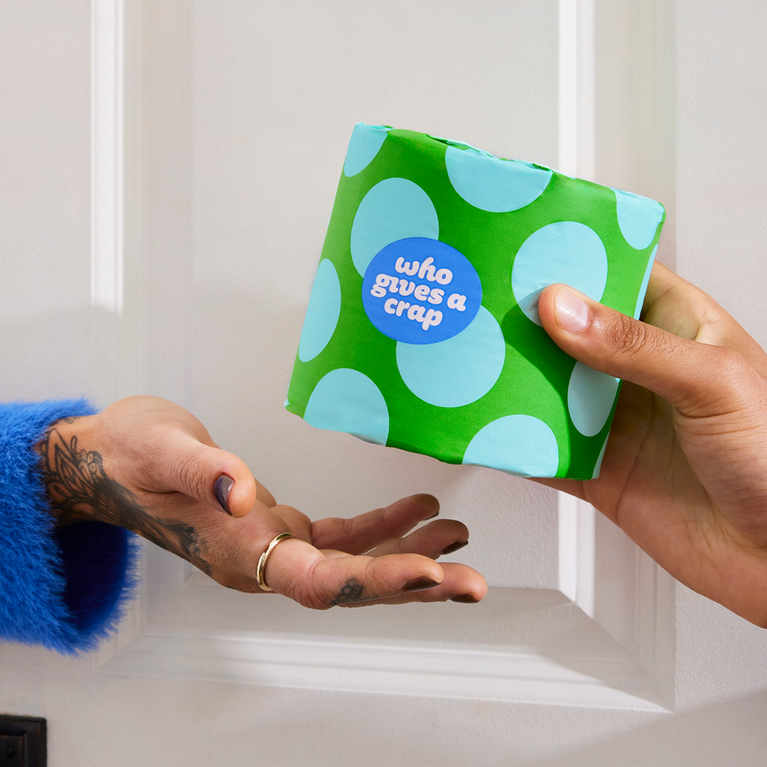 Hand reaching to shelf with colourfully wrapped eco-friendly toilet paper and tissue boxes.