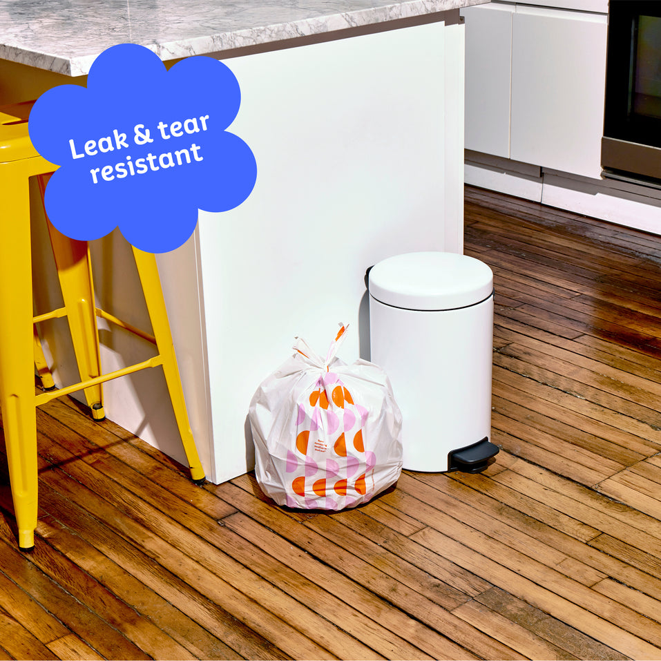 Who Gives a Crap small recycled garbage bag sits full next to kitchen bin. Caption in corner reads ‘Leak & tear resistant’.