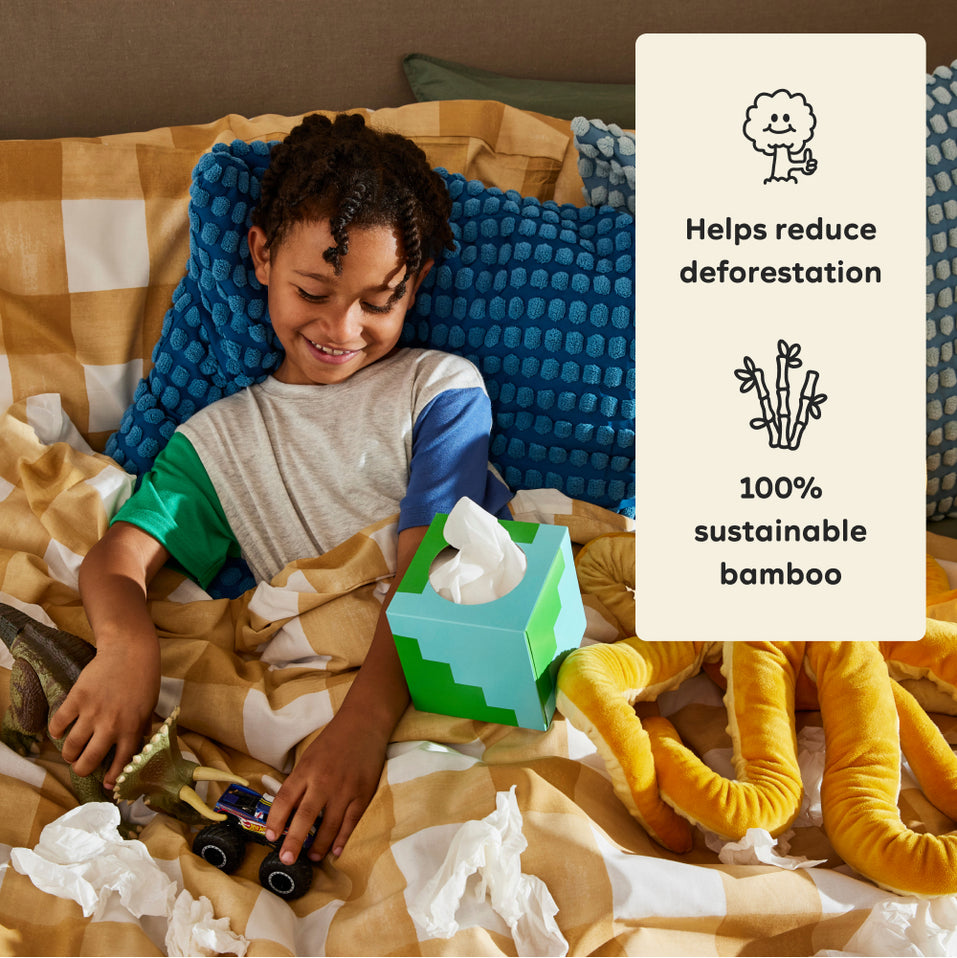 Young boy sits up in bed playing with toys with a box of Who Gives a Crap toilet paper beside him. Callout text reads ‘Helps reduce deforestation’ and ‘100% sustainable bamboo’.